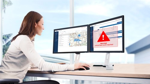 Eine Flottenmanagerin sitzt an ihrem Arbeitsplatz vor zwei Bildschirmen. Auf dem linken Bildschirm ist eine Landkarte zu erkennen, auf dem rechten Bildschirm wird eine Warnung in der VDO Software Tachograph Management angezeigt.